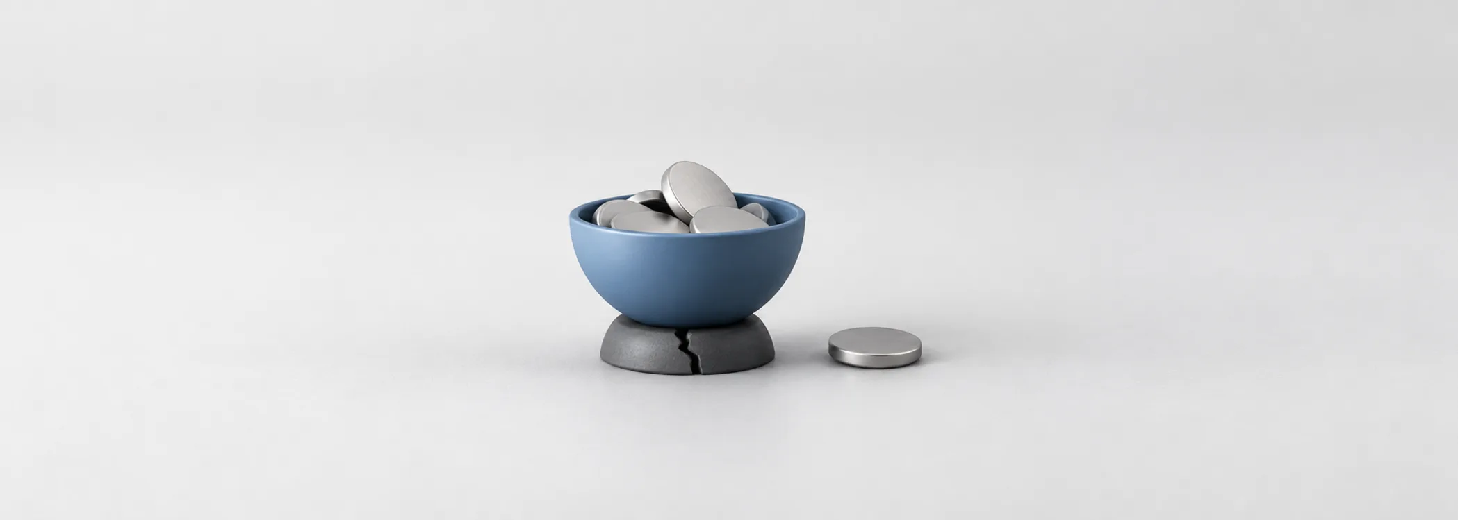 A steel-blue coin bowl on a cracked graphite support, with a loose silver coin, represents income resting on weak funding.